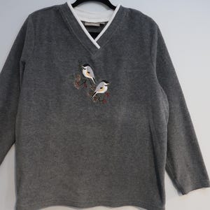 May include: Gray long-sleeved fleece sweater with a white v-neck and embroidered birds on the front.