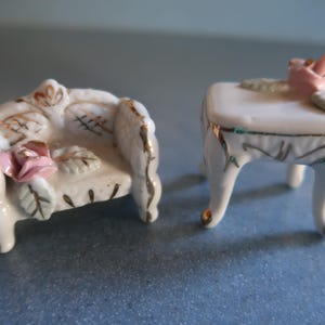May include: A miniature white porcelain sofa and table set with gold accents and pink rose decorations.
