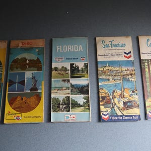 May include: A collection of vintage travel maps featuring destinations like Eastern United States, Ohio, Florida, San Francisco, and California. The maps have colorful illustrations and text, with the Sun Oil Company logo visible on some.