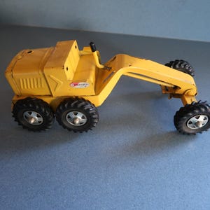 May include: Yellow toy grader with black wheels and a black steering wheel. The grader has a "Tonka" logo on the side.