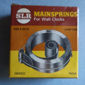 May include: A yellow and red box with the text "SLR Mainsprings For Wall Clocks" and "For 8 Days" printed on it. The box contains a coiled metal clock spring with a loop end.