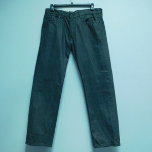 May include: A pair of dark gray jeans hanging on a hanger against a light blue wall.