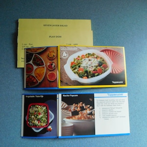 May include: A set of four recipe cards with yellow borders and blue text. The cards feature images of food and Tupperware containers. The recipes include Seven Layer Salad, Pasta Primavera, Vegetable Toss-Up, and Nacho Popcorn.