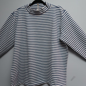 May include: A long-sleeved shirt with a mock neck, featuring horizontal stripes in navy blue and white. The shirt is hanging on a black hanger against a plain gray background. The fabric appears to be a medium weight.
