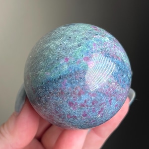 Peut inclure: Une sphère de pierre précieuse polie avec un mélange de teintes bleues, vertes et violettes. La sphère a un aspect moucheté avec une finition brillante, reflétant la lumière. La pierre précieuse est un objet décoratif.