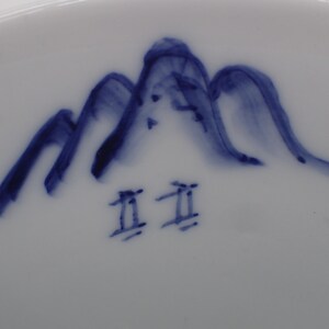 以下が含まれることがあります： 白地に青色の山と「工  工」の文字が描かれた白い陶器の皿のアップ写真です。