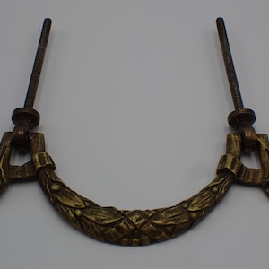 May include: A vintage brass drawer pull with a decorative floral design. The pull has two screws for attaching to a drawer.