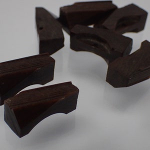 May include: A group of dark brown wooden puzzle pieces. The pieces are shaped like a curved arch and have a textured surface.