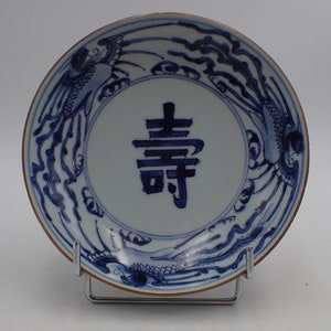 Peut inclure: Une assiette en porcelaine bleue et blanche avec un caractère chinois au centre et un motif de dragons stylisés autour du bord.