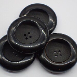 Peut inclure: Quatre boutons en plastique noir avec quatre trous chacun. Les boutons sont ronds et ont un bord surélevé.