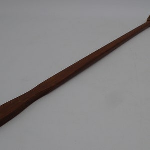 Puede incluir: Un rascador de espalda de madera con un extremo en forma de mano. El rascador es marrón y tiene un acabado liso.