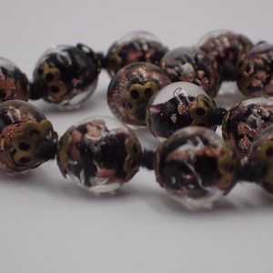 May include: A necklace made of clear glass beads with black and copper flecks. The beads are strung on a black cord and have a metallic finish.