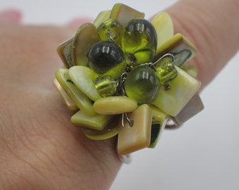 May include: A ring made of green and yellow beads and shells. The ring is made of a cluster of beads and shells, with a silver band.