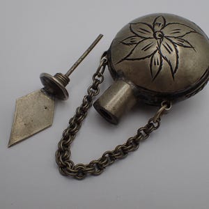 Può includere: Antica bottiglia di profumo argentata con un motivo floreale sul corpo sferico. La bottiglia include un tappo e una catena. Il tappo ha un'estremità a forma di diamante.