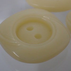 以下が含まれることがあります： 2つ穴のオフホワイトのプラスチックボタンが4つ。ボタンは縁に渦巻き模様があります。