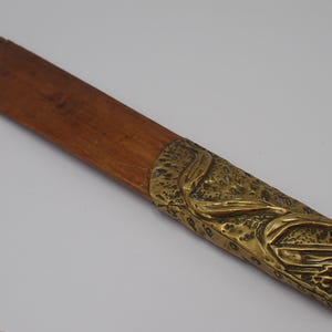 Peut inclure: Un coupe-papier composé d'une lame en bois brun, plate et lisse, et d'un manche en laiton moulé texturé. Le manche présente un motif organique en relief rappelant des feuilles, avec une finition antique patinée contrastant avec le bois.