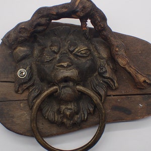 Può includere: Una targa in legno con un batacchio a testa di leone e un pezzo di legno di deriva attaccato alla parte superiore.