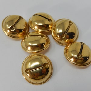 Puede incluir: Seis cascabeles dorados con una hendidura en la parte superior para colgar. Los cascabeles son brillantes y tienen una superficie lisa.