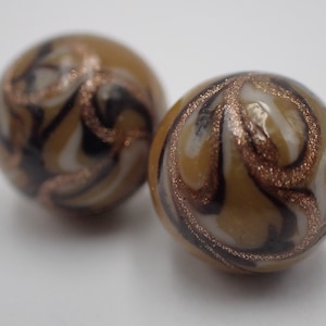 May include: Two round glass beads with a swirl pattern in brown, white, and gold. The beads have a glossy finish.