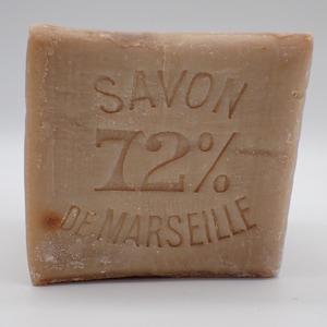 Op de afbeelding: Een rechthoekig stuk zeep in lichtbruin, met de woorden "SAVON 72% DE MARSEILLE" in reliëf op het oppervlak. De zeep heeft een handgemaakte uitstraling.