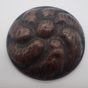 May include: A round, copper-coloured button with a raised, textured design of five rounded shapes.