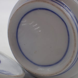 以下が含まれることがあります： 青と白の模様が施された白い陶器のボウル の底面。ボウルは円形で、滑らかで白い表面をしています。青い模様は同心円状の円です。