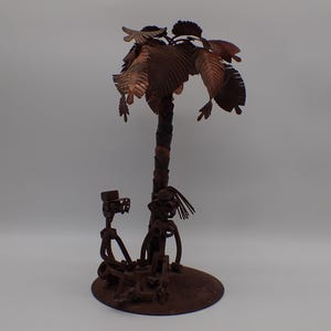 May include: A palm tree sculpture made from recycled metal. The tree is brown and has a rustic look. The sculpture is on a base that is also made of metal.