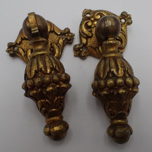 Op de afbeelding: Twee sierlijke messing kastgrepen met een decoratief bloemmotief en een ronde knop. De grepen zijn in vintage stijl en hebben een verweerde, antieke afwerking.