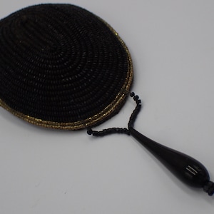 以下が含まれることがあります： 金色の縁取りと黒い涙型の取っ手を持つ、黒いビーズでできた手鏡です。