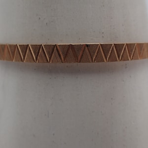 May include: A gold-toned bangle bracelet with a geometric pattern of triangles.