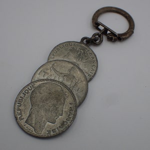 May include: A silver keychain with four French coins attached. The coins feature the text "REPUBLIQUE FRANCAISE" and various images.