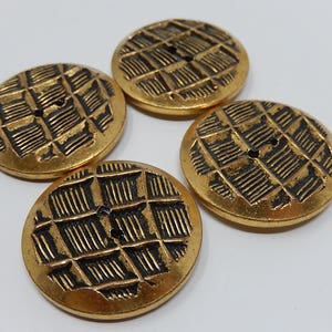 May include: Four gold-colored buttons with a black grid pattern. The buttons have two holes each.