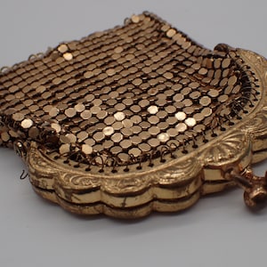 Könnte beinhalten: Eine goldene Netz-Handtasche mit einem dekorativen Verschluss. Die Tasche besteht aus kleinen, runden Metallgliedern.