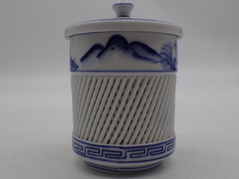 以下が含まれることがあります： 青と白の山を描いた白い陶器の壺。蓋と中央に格子模様がある。