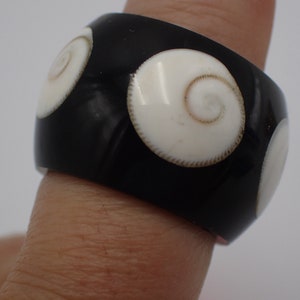 Peut inclure: Une bague noire avec des incrustations de coquillages blancs. Les incrustations de coquillages ont un motif en spirale.