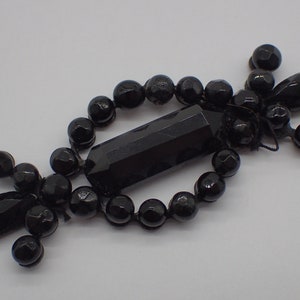 Peut inclure: Bijou en perles de verre et cristal noir avec un long cristal rectangulaire au centre. La pièce est faite de perles de verre et de cristaux noirs, et elle a un design délicat et complexe.