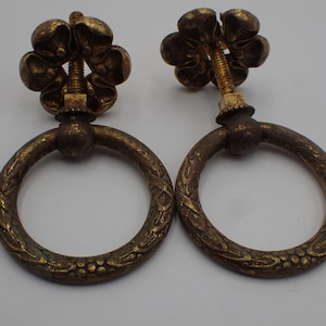 Op de afbeelding: Twee antieke messing ringgrepen met een bloemmotief. Elke greep heeft een ronde ring met een decoratief bloemmotief en een schroefdop met een bloemmotief.