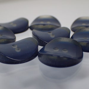 Op de afbeelding: Acht donkerblauwe, plastic knopen met twee gaten en een licht doorschijnende, iriserende afwerking. De knopen zijn gevormd als een afgerond rechthoek met een lichte bocht aan één kant.