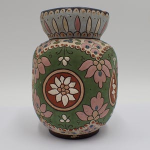 以下が含まれることがあります： 緑色のベースにピンクと白の花柄が施された陶器の花瓶。花瓶は首の周りに詳細なデザインがあり、茶色のベースがあります。 全体的な美しさはヴィンテージで装飾的です。