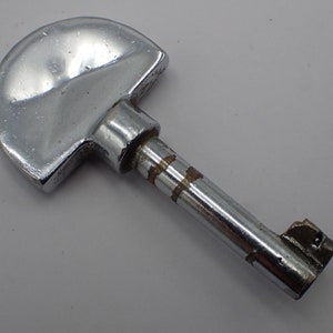 Peut inclure: Une clé argentée avec une grosse tête arrondie en demi-cercle et un long manche droit. Le manche est orné de deux fines lignes horizontales gravées.