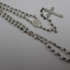 May include: A white rosary with a silver chain and a silver cross pendant.