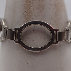 Op de afbeelding: Een zilveren armband met een kettingschakelontwerp en ovale schakels. De armband is gemaakt van metaal en heeft een gepolijste afwerking.