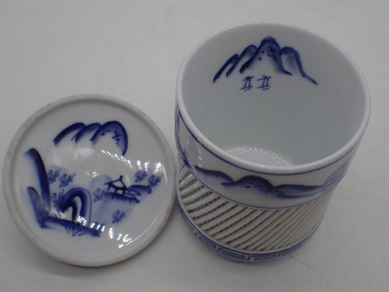 以下が含まれることがあります： 青と白の山の風景のデザインが施された、白磁の茶碗と蓋。茶碗の底には格子模様があり、内側には「五五」の文字が書かれている。