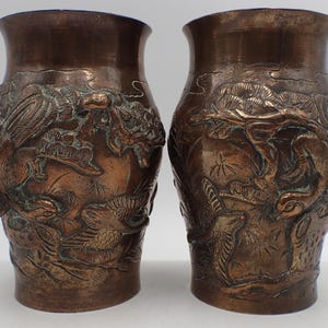 Peut inclure: Deux vases de couleur bronze avec des sculptures en relief détaillées. Les vases ont une base large et un bord légèrement évasé. Le relief représente des oiseaux, des dragons et du feuillage. Ce sont probablement des objets décoratifs.