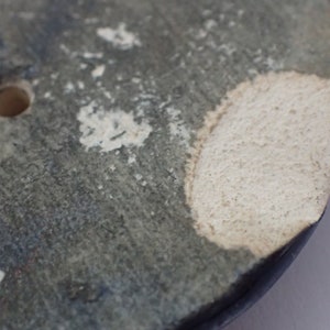 Pu&ograve; includere: Primo piano di un vaso in ceramica blu scuro con una glassa bianca. Il vaso ha un bordo scheggiato e due fori sul lato.