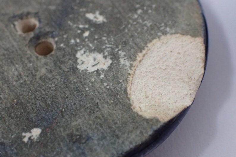 Pu&ograve; includere: Primo piano di un vaso in ceramica blu scuro con una glassa bianca. Il vaso ha un bordo scheggiato e due fori sul lato.