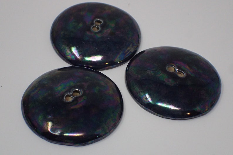 Pu&ograve; includere: Tre bottoni neri iridescenti con un solo foro ciascuno. I bottoni hanno una superficie liscia e arrotondata e un bordo leggermente rialzato.