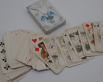 May include: An antique deck of playing cards with a decorative box. The cards are fanned out, revealing illustrations and traditional suits. The box is white with blue floral and dragon-like designs, and the text "B-D" is visible.