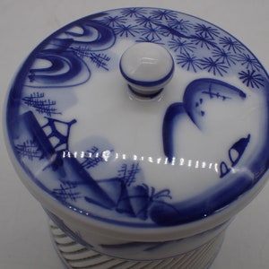 以下が含まれることがあります： 青と白のフラワーデザインが施された白い陶器の壺。蓋の上にはノブがあり、青と白のフラワーデザインが施されています。壺の底にはリブ模様があります。