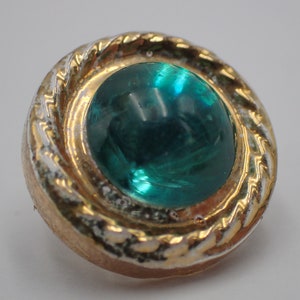May include: A round, gold-coloured button with a raised, twisted rim and a large, green glass cabochon in the centre.